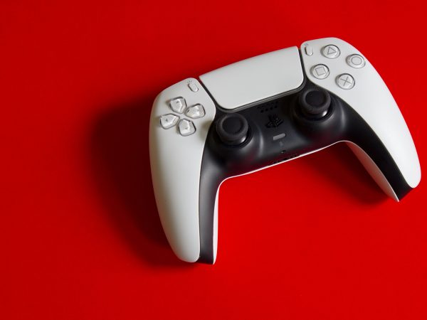 Witte PlayStation 5 DualSense controller van bovenaf gefotografeerd op een felrode achtergrond, met duidelijk zicht op de knoppen en joysticks