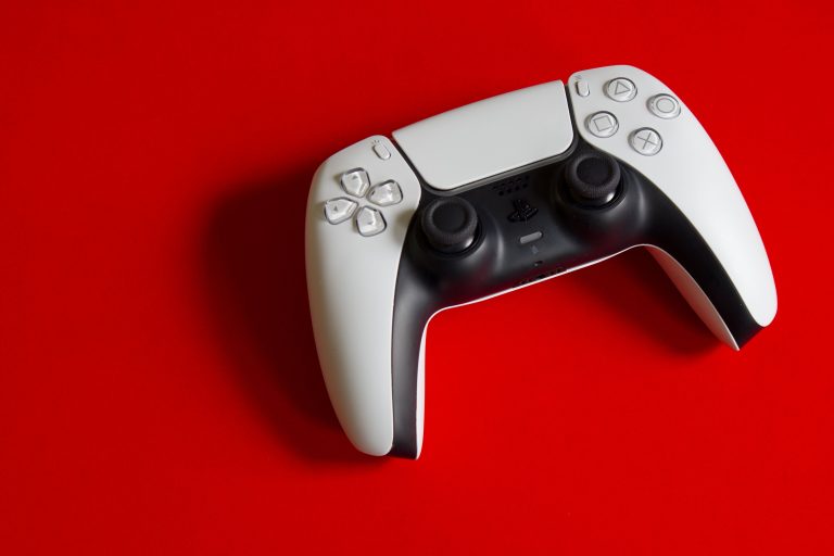 Witte PlayStation 5 DualSense controller van bovenaf gefotografeerd op een felrode achtergrond, met duidelijk zicht op de knoppen en joysticks