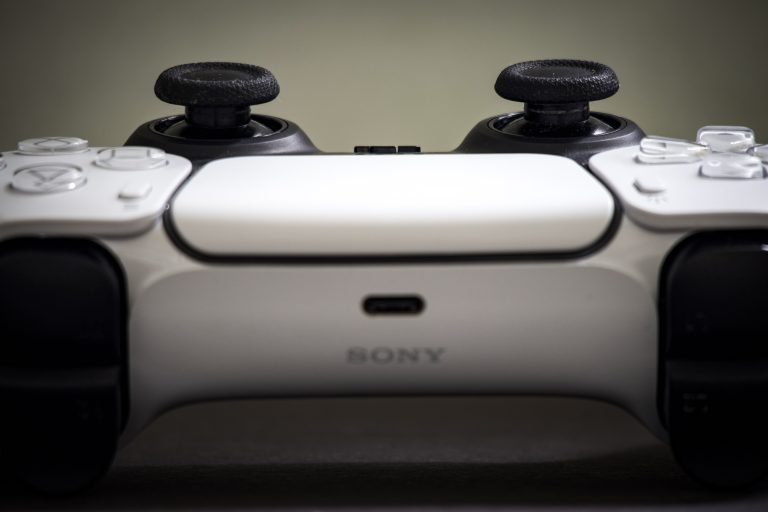 Frontale macro opname van een witte PlayStation DualSense controller, met de twee joysticks bovenaan en het Sony logo in het midden
