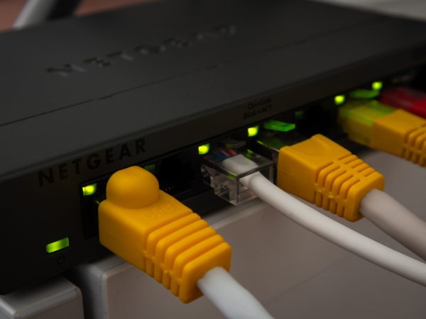 Zwarte Netgear netwerkswitch met gele, witte en rode netwerkkabels en groene lampjes van dichtbij