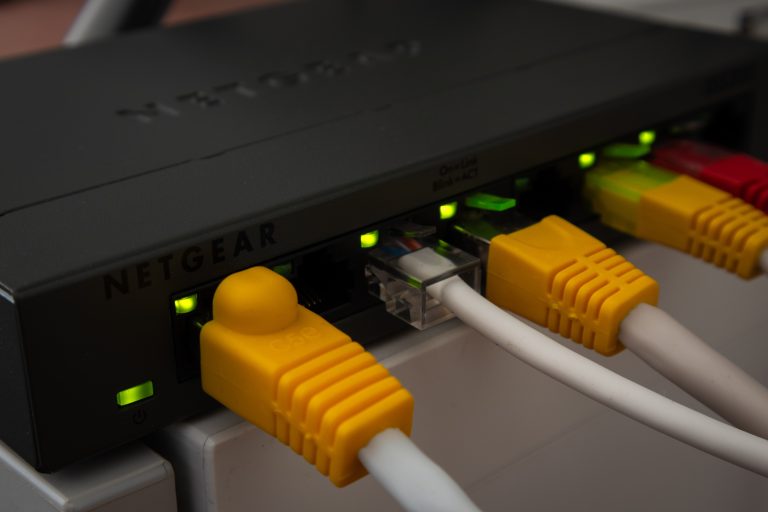 Zwarte Netgear netwerkswitch met gele, witte en rode netwerkkabels en groene lampjes van dichtbij