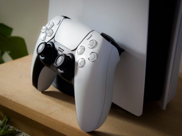 Sony PlayStation 5 controller leunend tegen de console op houten plank