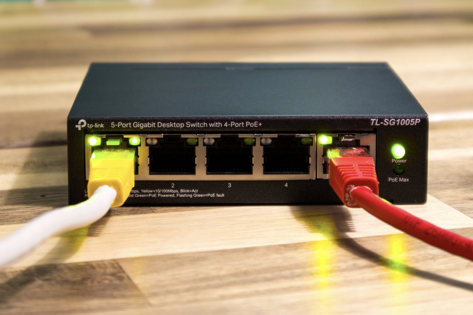 Zwarte TP-Link TL-SG1005P netwerkswitch met een gele en een rode netwerkkabel op een houten tafel
