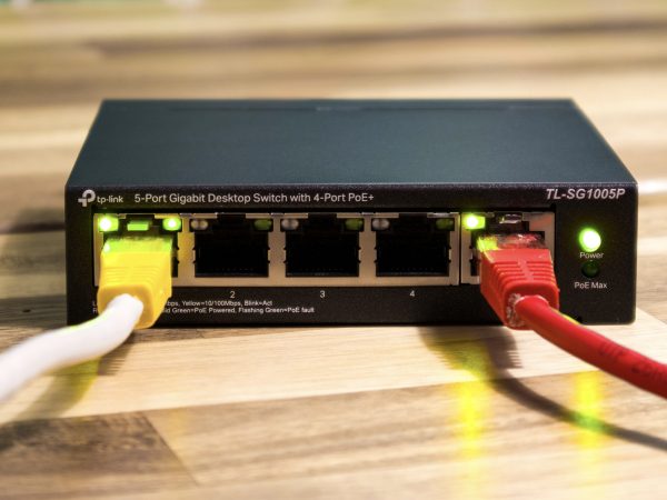 Zwarte TP-Link TL-SG1005P netwerkswitch met een gele en een rode netwerkkabel op een houten tafel