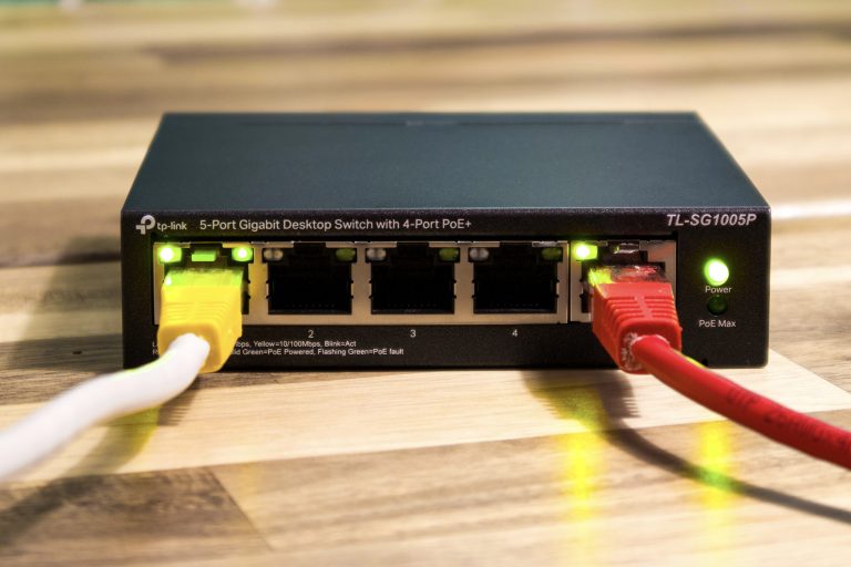 Zwarte TP-Link TL-SG1005P netwerkswitch met een gele en een rode netwerkkabel op een houten tafel